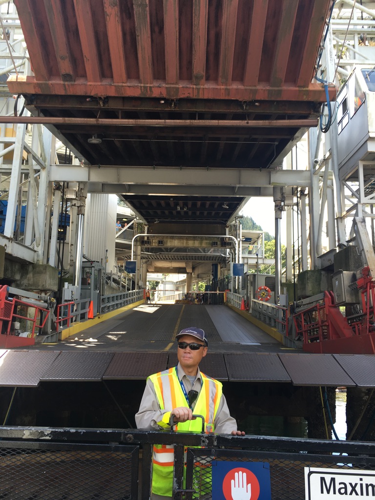 A ferry worker in a safety vest is ready to open a gate and let cars of a ferry docking at horseshoe Bay